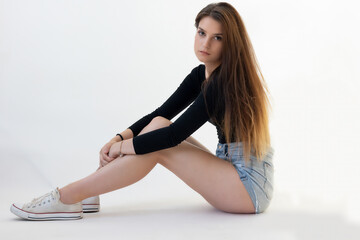 Young long legged woman is posing on floor on the light bacground. The girl is looking at the...