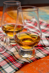 Tulip-shaped tasting glass with dram of Scotch single malt or blended whisky on wooden table with tartan