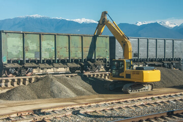 Unloading unloading rubble with an excavator wagons with bulk cargo gravel, sand at the station.