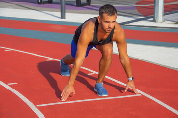 Young male athlete getting ready to sprint down the track at an athletics event on a bright, sunny...