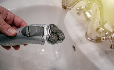 Cleaning the electric shaver mesh under running water in the faucet. Clean the beard shaving...
