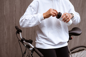 Faceless shot of african american woman in hoodie holding sports bottle near bicycle on street 