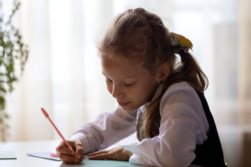The cute girl at the table is doing her homework.A child in a school uniform at home.The schoolgirl...