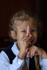Portrait of a blonde girl in a school uniform,who smiles and looks into the camera.Return to school and Knowledge Day.A happy child is playing with a pen.Photography in a dark key
