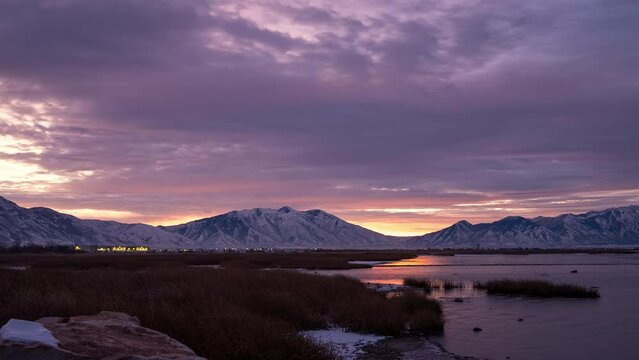 Sunrise timelapse with colorful sky lighting up and the sun peaking over the mountains covered in snow where the Provo River flows into Utah Lake.