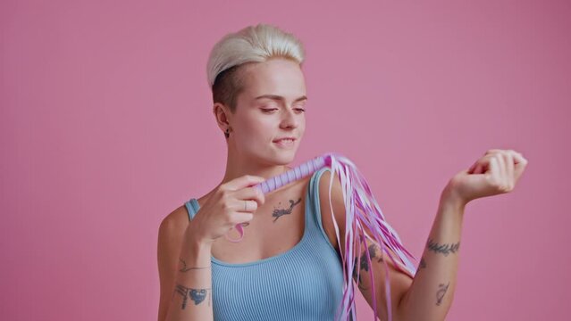 Excited playful woman holding pink whip in hands and playing mistress and slave