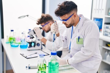 Young couple wearing scientist uniform using microscope and pipette at laboratory
