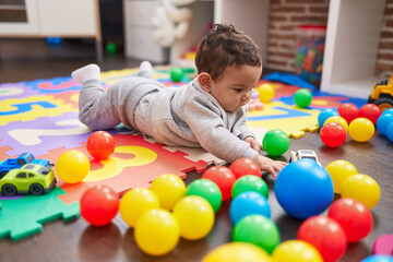 Fototapeta na wymiar Adorable hispanic baby playing with balls lying on floor at kindergarten