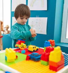 Adorable toddler playing with construction blocks standing at kindergarten