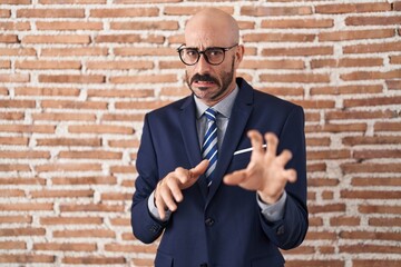 Bald man with beard wearing business clothes and glasses disgusted expression, displeased and fearful doing disgust face because aversion reaction. with hands raised