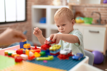 Adorable toddler playing with car and toy and construction blocks sitting on table at kindergarten