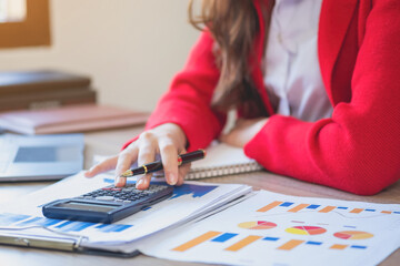 Marketing, finance, accounting, planning, a slender female accountant in a red suit using a laptop calculator and documents, charts, and graphs in company profit analysis. Business idea