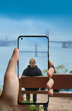 Taking a picture with a mobile phone of a women sitting on a bench watching the Golden Gate Bridge in San Francisco, USA.