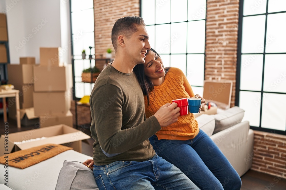 Wall mural Man and woman couple smiling confident drinking coffee at new home