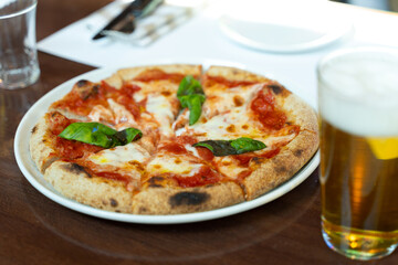 Hot pizza in a white plate and fresh beer on a wooden table thin crust pizza Italian