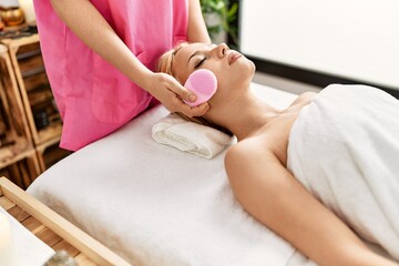 Obraz na płótnie Canvas Young caucasian woman lying on table having skin face treatment using machine at beauty salon