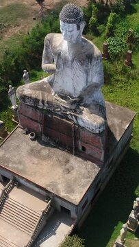 Vertical video of Drone footage of the north part of Battambang. The camera is facing down at a massive buddha statue 20m tall in the Ek Phnom Temple area and is turning around it 90 degrees keeping t