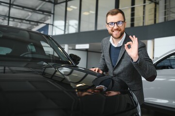 Visiting car dealership. Handsome bearded man is stroking his new car and smiling