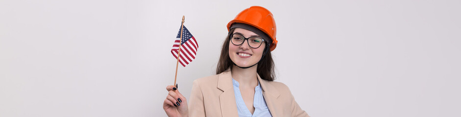 A girl in a construction helmet and an American flag stands happy on a white background.