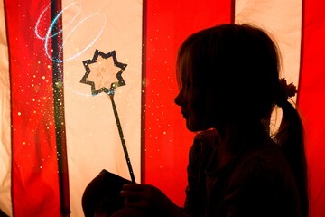 silhouette of a sitting little girl casting a spell with a magic wand in front of a circus tent	