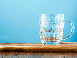 Empty massive beer glass jar on a wooden table. Blue background.