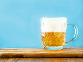 Beer mug half full and tall froth. Lager in a glass. Blue wall background. Copy space.