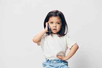 a cute little preschool girl is standing on a white background in a white T - shirt sitting on a chair talking on the phone with one hand on her hip . The topic of children's conversation