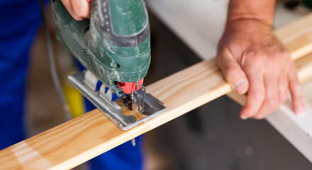 Closeup of hands using a jigsaw machine on wooden plank at the workshop, banner