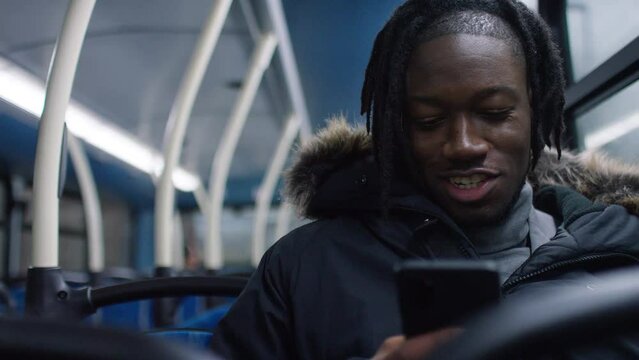 Young man smiles on his phone as he sits on the bus, with space for text, in slow motion 