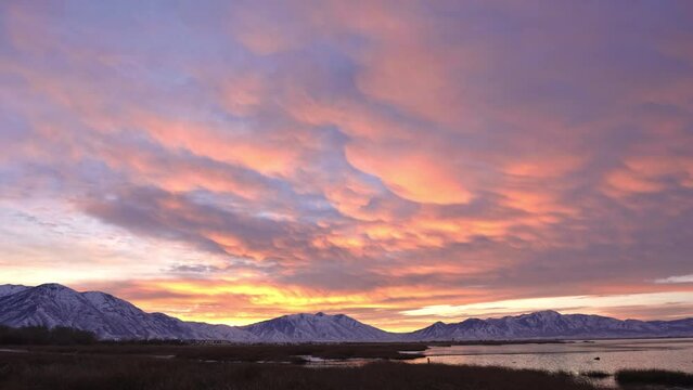 Panning view of colorful sunrise along Utah Lake in winter with snow capped mountains.