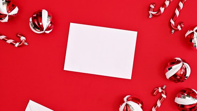 Christmas card with opening envelope with white paper on red background with ornaments. Stop motion. Flat lay