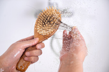 A woman suffering from alopecia is looking at hair caught on a comb while taking a shower