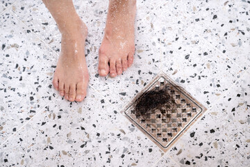 A woman suffering from alopecia is taking a shower, there is hair in the drain next to her feet