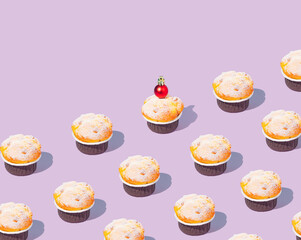 Creative pattern made of cupcake decorated with shiny red Christmas bauble. Trendy concept, collage on a purple pastel background. Creative art minimal aesthetic. Copy space.