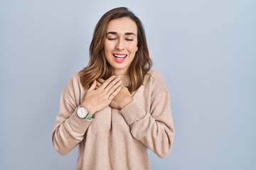 Young woman standing over isolated background smiling with hands on chest with closed eyes and grateful gesture on face. health concept.