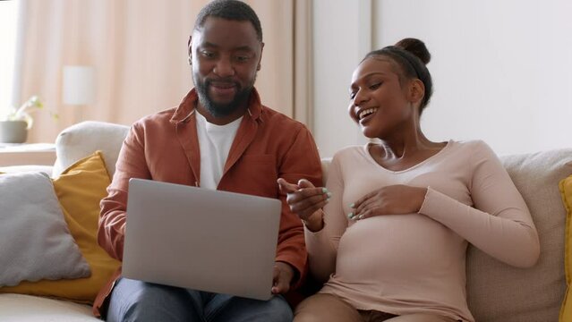 Prenatal online shopping. Young happy pregnant african american woman and her husband web surfing on laptop, free space