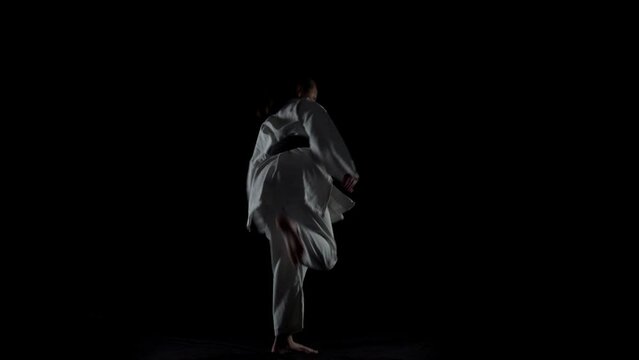 Young girl wearing kimono and practicing karate against black background