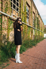 Young girl with cool outfit standing in front of an abandoned building with vegetation in the exterior
