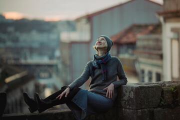 Fototapeta na wymiar A woman sits on an ancient stone wall in Porto downtown, Portugal.
