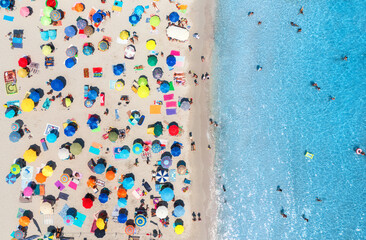 Aerial view of colorful umbrellas on sandy beach, swimming people in blue sea at sunset in summer...