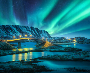 Bridge and northern lights over snowy mountains. Lofoten islands, Norway. Aurora borealis and...