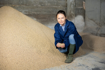 Woman farmer squatting at heap of soybean husk in fodder storage.