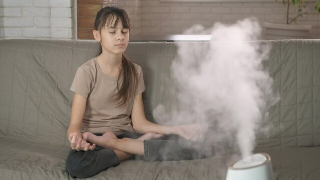 Doing yoga in air purifier. A young girl doing yoga exercices on the sofa by the air arona purifier in the room.