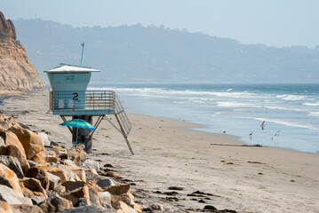 View of lifeguard hut on sandy beach and scenic view of waves splashing in sea with mountain and clear sky in the background at San Diego during sunny day