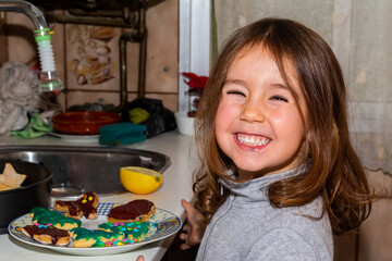 Caucasian brown-haired little girl cooking gingerbread cookies in the kitchen. Girl decorating Christmas cookies. Games in the kitchen. Christmas foods.