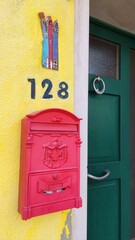 Pink mailbox on a yellow wall, next to a green door, on the island of Burano, Italy. Local flavor and traditions on the Venetian island of Burano