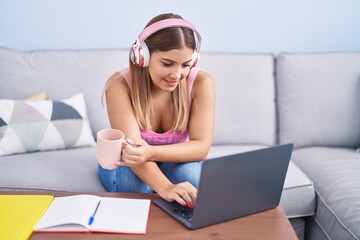 Young beautiful hispanic woman student listening to music drinking coffee at home