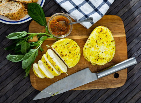 Slices of spicy roasted cottage cheese seasoned with turmeric and cumin seeds on wooden cutting board served with whole-grain baguette and greens. Healthy breakfast concept