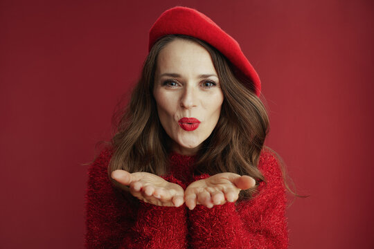 smiling modern woman in red sweater and beret blowing air kiss
