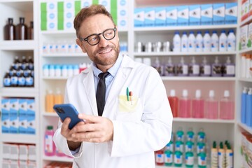 Middle age man pharmacist using smartphone working at pharmacy